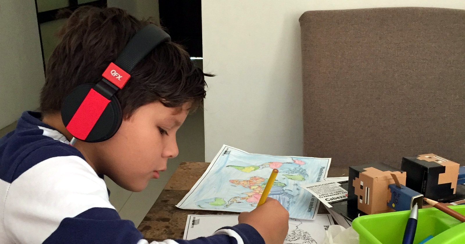 Niño haciendo homeschool en la mesa de su casa, coloreando un mapa del mundo